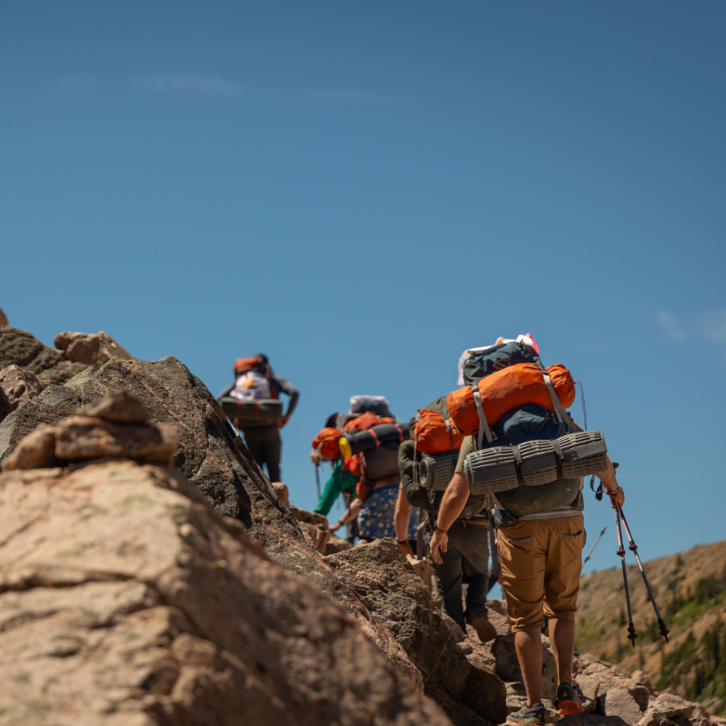 A group of people hiking up a rock formation away from the camera. Hikers are wearing backpacks and holding trekking poles.