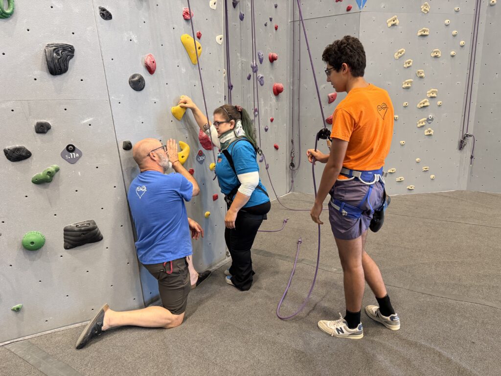 A climber learns how to approach an indoor climbing gym rock wall using adaptive equipment.